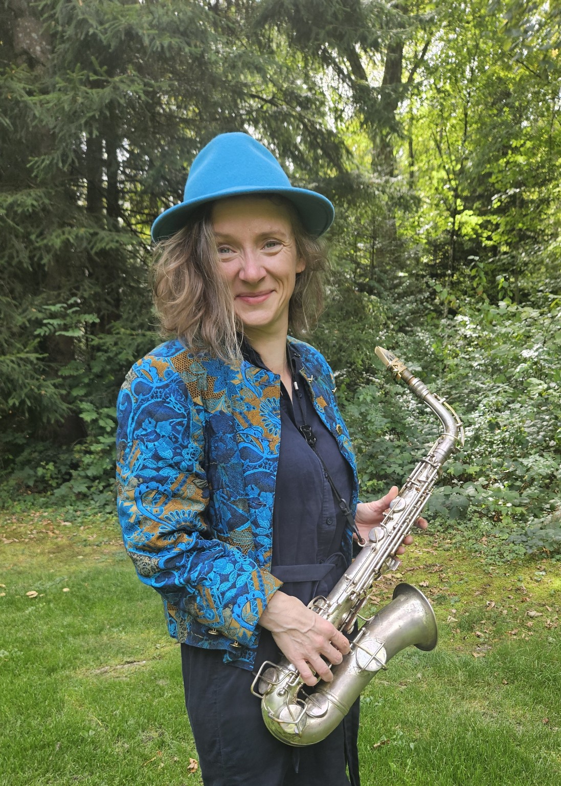 Stefanie Grass mit blauem Hut und Saxophon im Grünen
